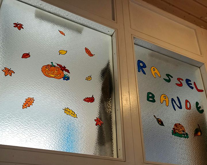 Glastür mit dem bunten Schriftzug Rasselbande und herbstlichen Fensterbildern
